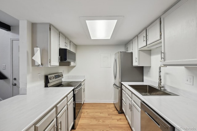 kitchen featuring appliances with stainless steel finishes, a sink, light countertops, light wood-type flooring, and baseboards