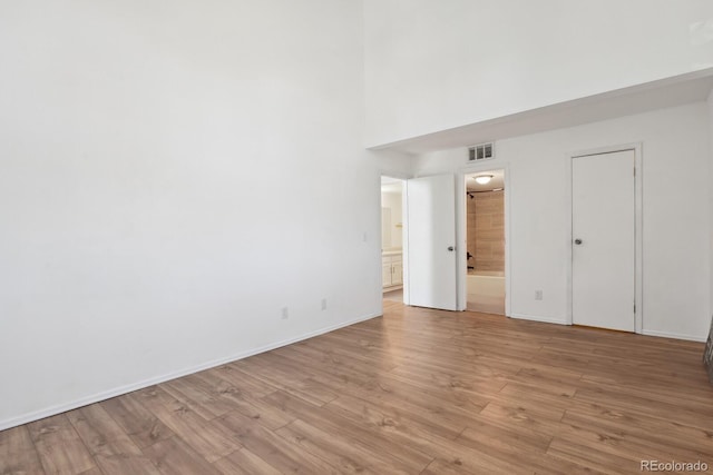 empty room featuring light wood-style floors, a high ceiling, and baseboards