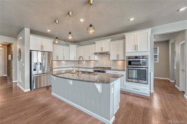23957 E Rocky Top Ave, Aurora, CO 80016 - kitchen featuring stainless steel appliances, under cabinet range hood, white cabinetry, a breakfast bar area, and a textured ceiling
