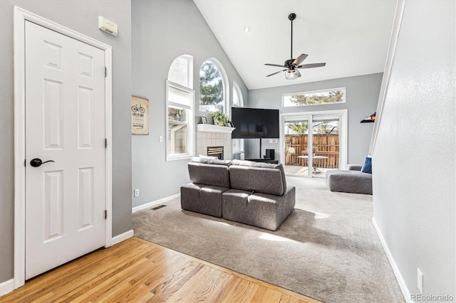 living room featuring ceiling fan, high vaulted ceiling, a tiled fireplace, and hardwood / wood-style flooring