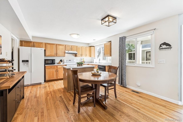 kitchen with black appliances, a kitchen island, wooden counters, light wood-type flooring, and sink