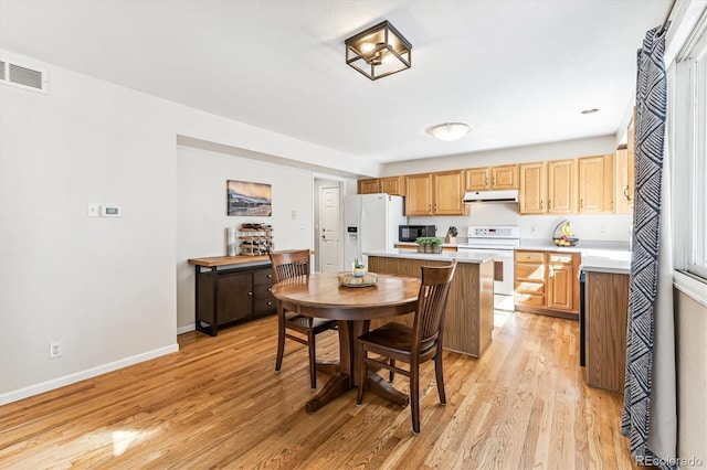 kitchen with white appliances, light wood-type flooring, and a kitchen bar