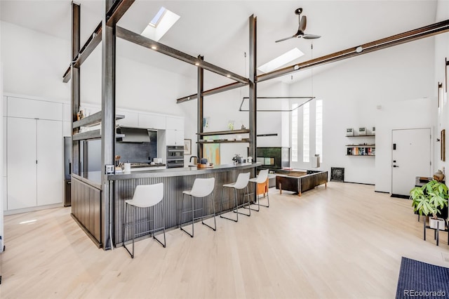 2801 Lawrence St, Denver, CO 80205 - kitchen with high vaulted ceiling, a skylight, white cabinets, a breakfast bar, and light wood finished floors