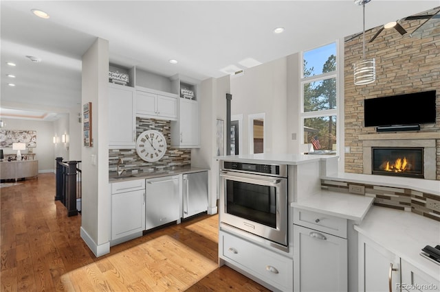 kitchen with white cabinetry, decorative backsplash, hanging light fixtures, stainless steel appliances, and light wood-type flooring