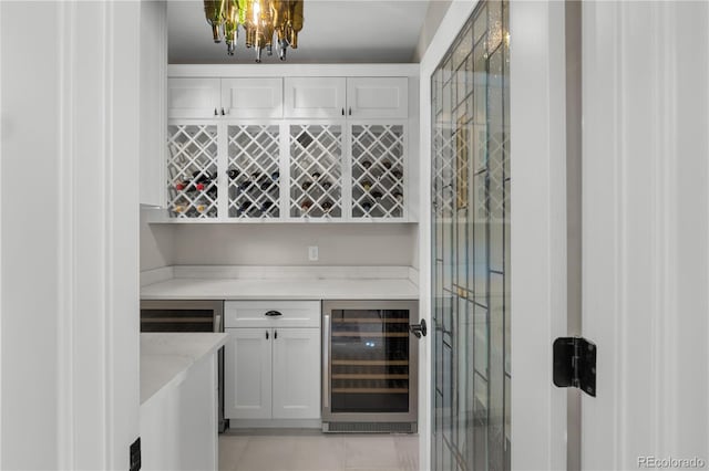 bar featuring wine cooler, an inviting chandelier, light stone counters, light tile patterned floors, and white cabinets