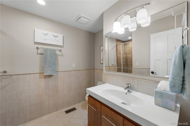 bathroom with a shower with door, tile walls, vanity, tile patterned floors, and toilet