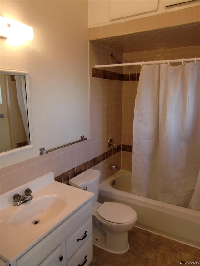 full bathroom with shower / tub combo with curtain, tile walls, tile patterned flooring, vanity, and toilet