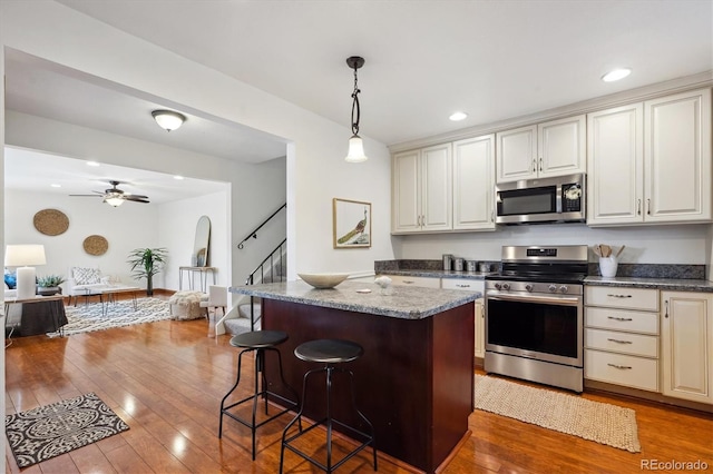 kitchen featuring open floor plan, a kitchen bar, hardwood / wood-style flooring, hanging light fixtures, and stainless steel appliances