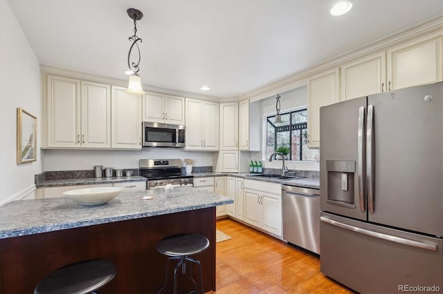 kitchen with a kitchen breakfast bar, decorative light fixtures, a sink, light wood-style floors, and stainless steel appliances