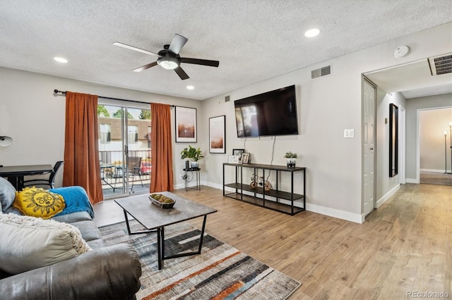 living area featuring light wood-type flooring, visible vents, a textured ceiling, and baseboards