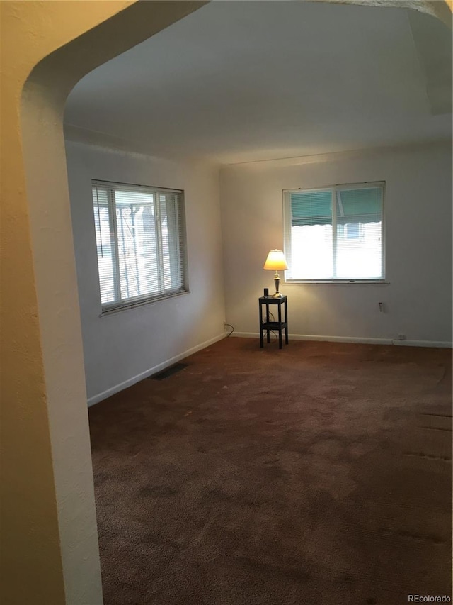 spare room featuring baseboards, visible vents, dark colored carpet, and a wealth of natural light