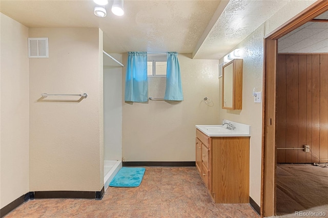 bathroom featuring visible vents, baseboards, a textured ceiling, a shower stall, and vanity