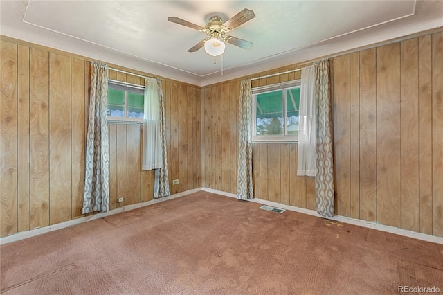 spare room with wood walls, carpet flooring, visible vents, and ceiling fan