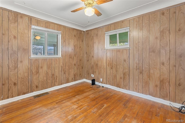 empty room featuring baseboards, a ceiling fan, wood walls, visible vents, and hardwood / wood-style floors