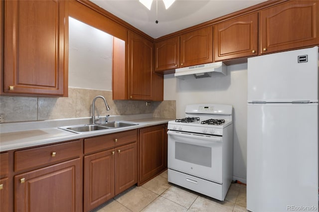 kitchen with white appliances, light countertops, under cabinet range hood, brown cabinets, and a sink