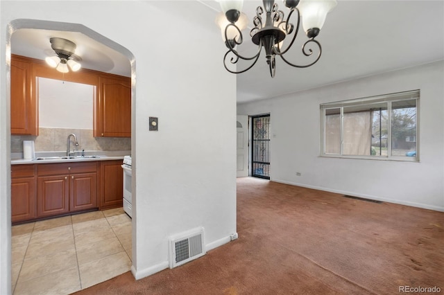 kitchen featuring visible vents, light carpet, light countertops, a sink, and decorative backsplash