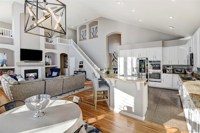 kitchen with light stone countertops, appliances with stainless steel finishes, a towering ceiling, decorative light fixtures, and white cabinetry