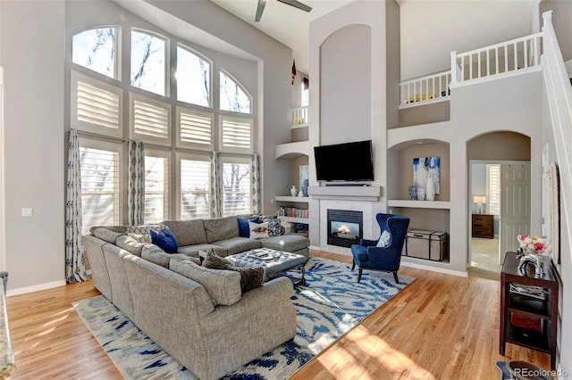 living room featuring a tiled fireplace, built in features, light hardwood / wood-style floors, and a high ceiling