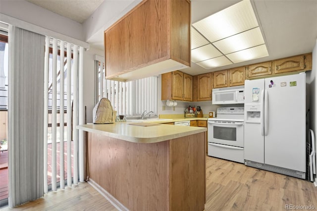 kitchen featuring a wealth of natural light, white appliances, kitchen peninsula, and light hardwood / wood-style floors