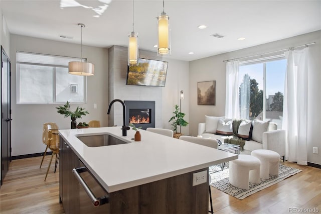 kitchen featuring a large fireplace, visible vents, light countertops, light wood-type flooring, and a sink