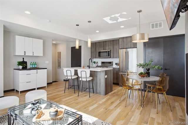 kitchen featuring stainless steel appliances, visible vents, light wood finished floors, modern cabinets, and a kitchen bar