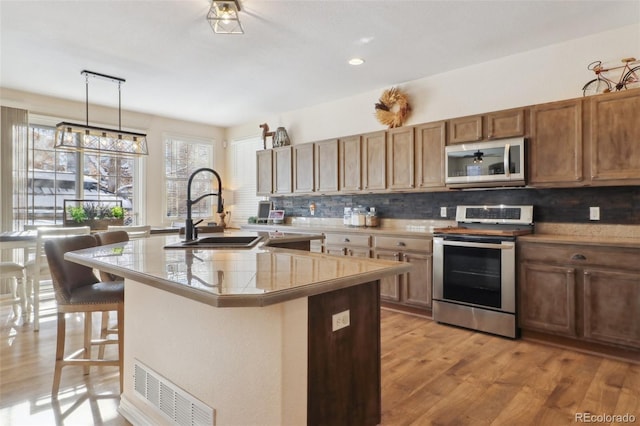 kitchen with hanging light fixtures, appliances with stainless steel finishes, sink, a kitchen bar, and an island with sink