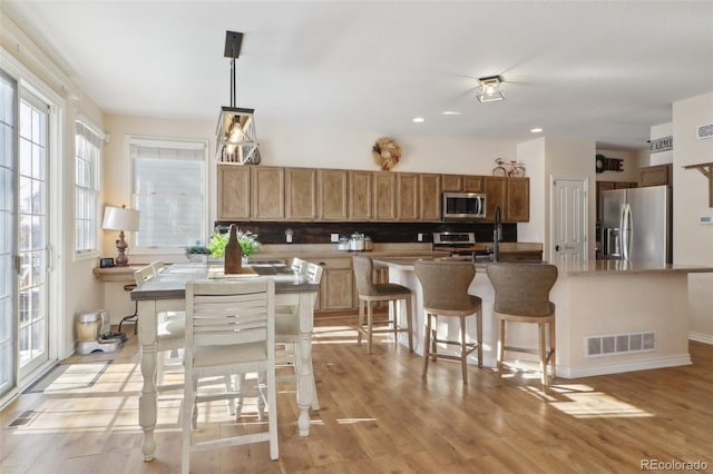 kitchen featuring a kitchen island, stainless steel appliances, backsplash, hanging light fixtures, and light wood-type flooring