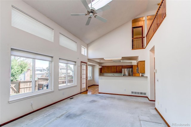 unfurnished living room with high vaulted ceiling, light colored carpet, baseboards, and ceiling fan