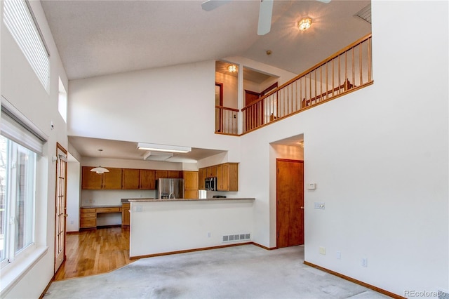 unfurnished living room with high vaulted ceiling, ceiling fan, baseboards, and light carpet