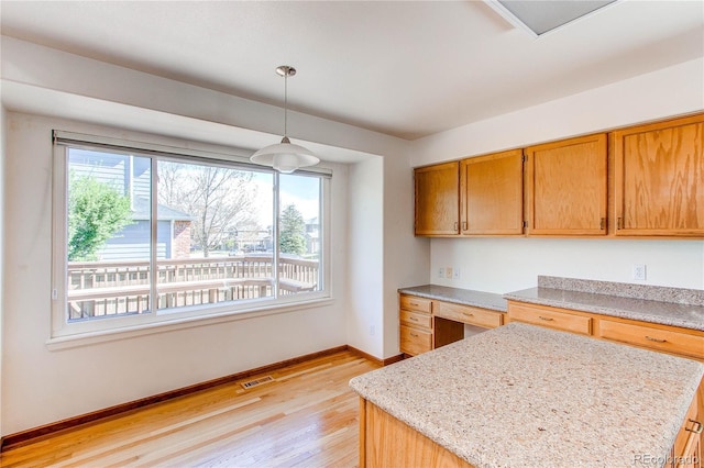kitchen featuring baseboards, light wood-style floors, decorative light fixtures, built in desk, and light stone counters