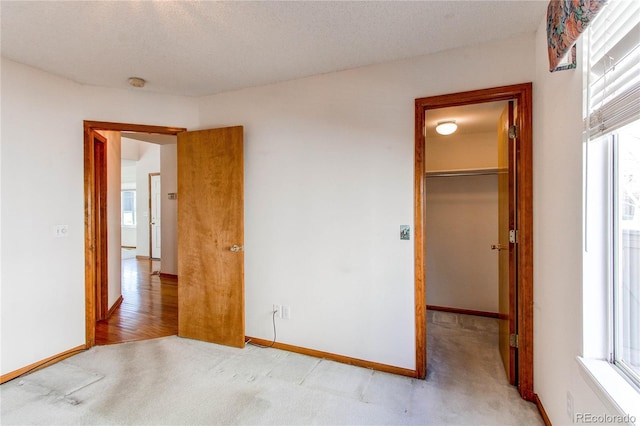 unfurnished bedroom with a walk in closet, light colored carpet, multiple windows, and baseboards