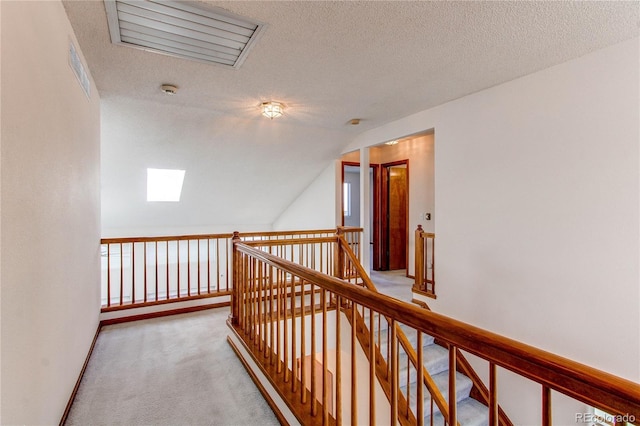 hall with an upstairs landing, carpet floors, lofted ceiling, a textured ceiling, and a skylight