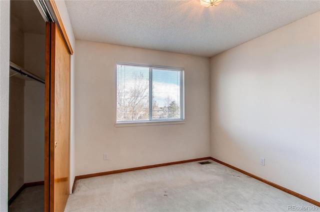 unfurnished bedroom with a closet, a textured ceiling, light carpet, and baseboards