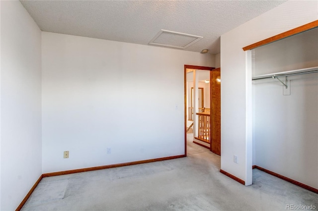 unfurnished bedroom featuring carpet, a closet, attic access, baseboards, and a textured ceiling