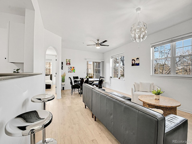 living room featuring light wood-style floors, baseboards, arched walkways, and ceiling fan with notable chandelier