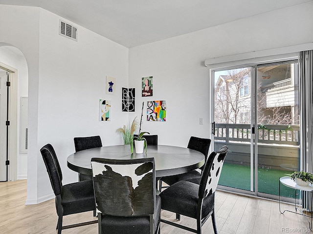 dining room with light wood-type flooring, baseboards, visible vents, and arched walkways