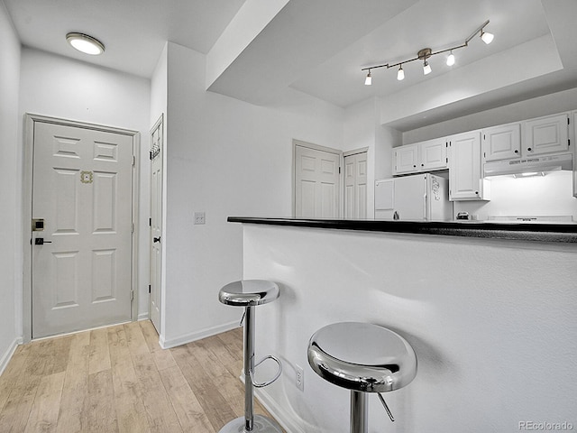 kitchen with white cabinets, light wood-style floors, dark countertops, refrigerator, and under cabinet range hood