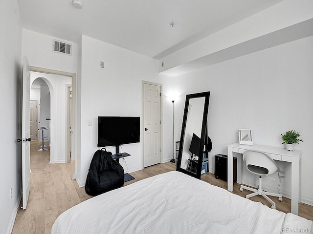 bedroom with arched walkways, baseboards, visible vents, and light wood-style floors