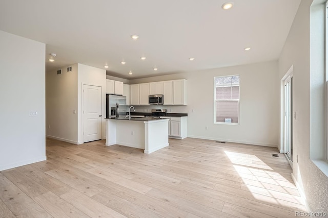 kitchen featuring sink, appliances with stainless steel finishes, white cabinets, a center island with sink, and light wood-type flooring