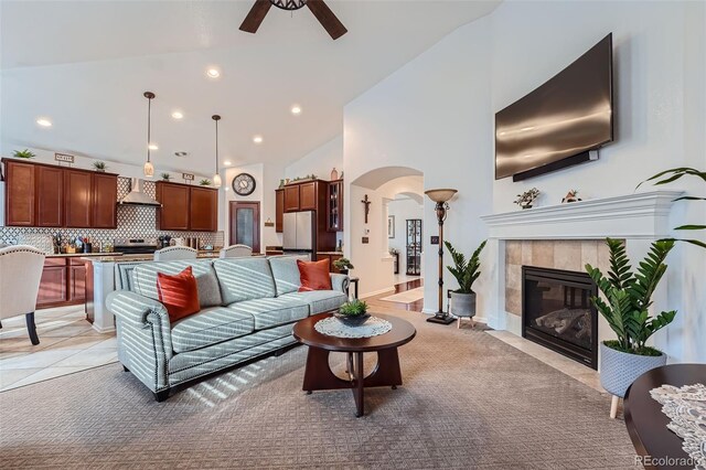 living room with high vaulted ceiling, ceiling fan, a tile fireplace, and light tile patterned floors