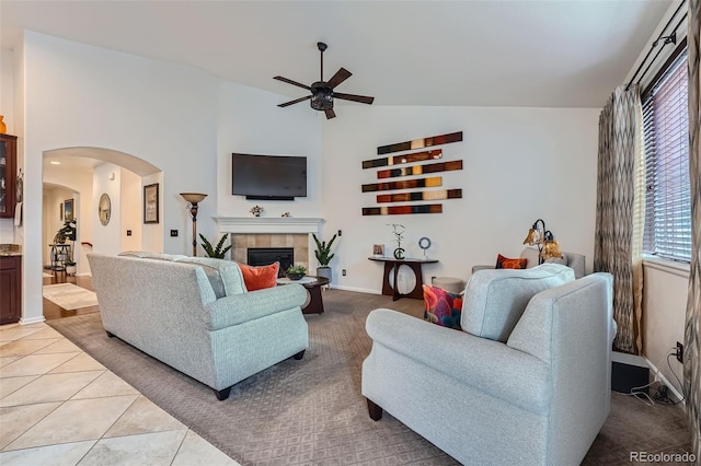 tiled living room with ceiling fan, a tiled fireplace, and high vaulted ceiling