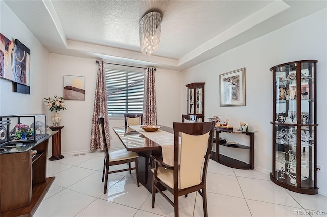 dining area with a tray ceiling, a chandelier, and light tile patterned floors