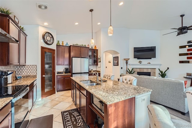 kitchen with ceiling fan, white refrigerator, an island with sink, sink, and a tiled fireplace