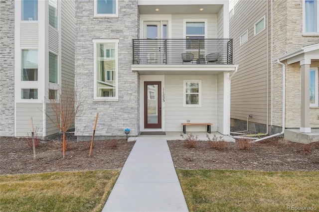 view of exterior entry featuring stone siding and a balcony