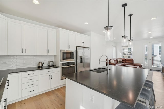 kitchen featuring light wood finished floors, a sink, appliances with stainless steel finishes, dark countertops, and backsplash