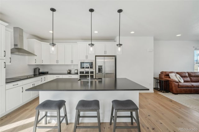 kitchen featuring a sink, stainless steel appliances, dark countertops, wall chimney exhaust hood, and light wood-type flooring