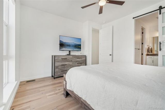 bedroom featuring connected bathroom, a barn door, light wood-style floors, baseboards, and ceiling fan