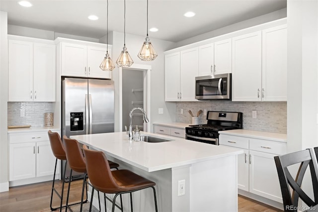 kitchen featuring stainless steel appliances, sink, white cabinets, light hardwood / wood-style floors, and an island with sink