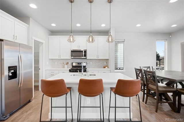 kitchen with sink, hanging light fixtures, light hardwood / wood-style flooring, a center island with sink, and appliances with stainless steel finishes