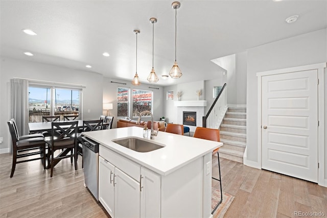 kitchen with dishwasher, sink, an island with sink, pendant lighting, and white cabinets